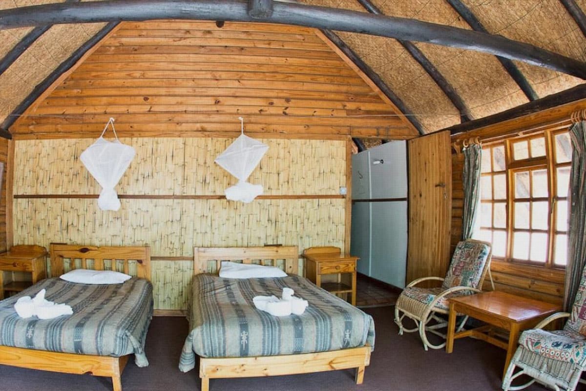 A log cabin room with two beds, a wooden desk, a chair, and a refrigerator.