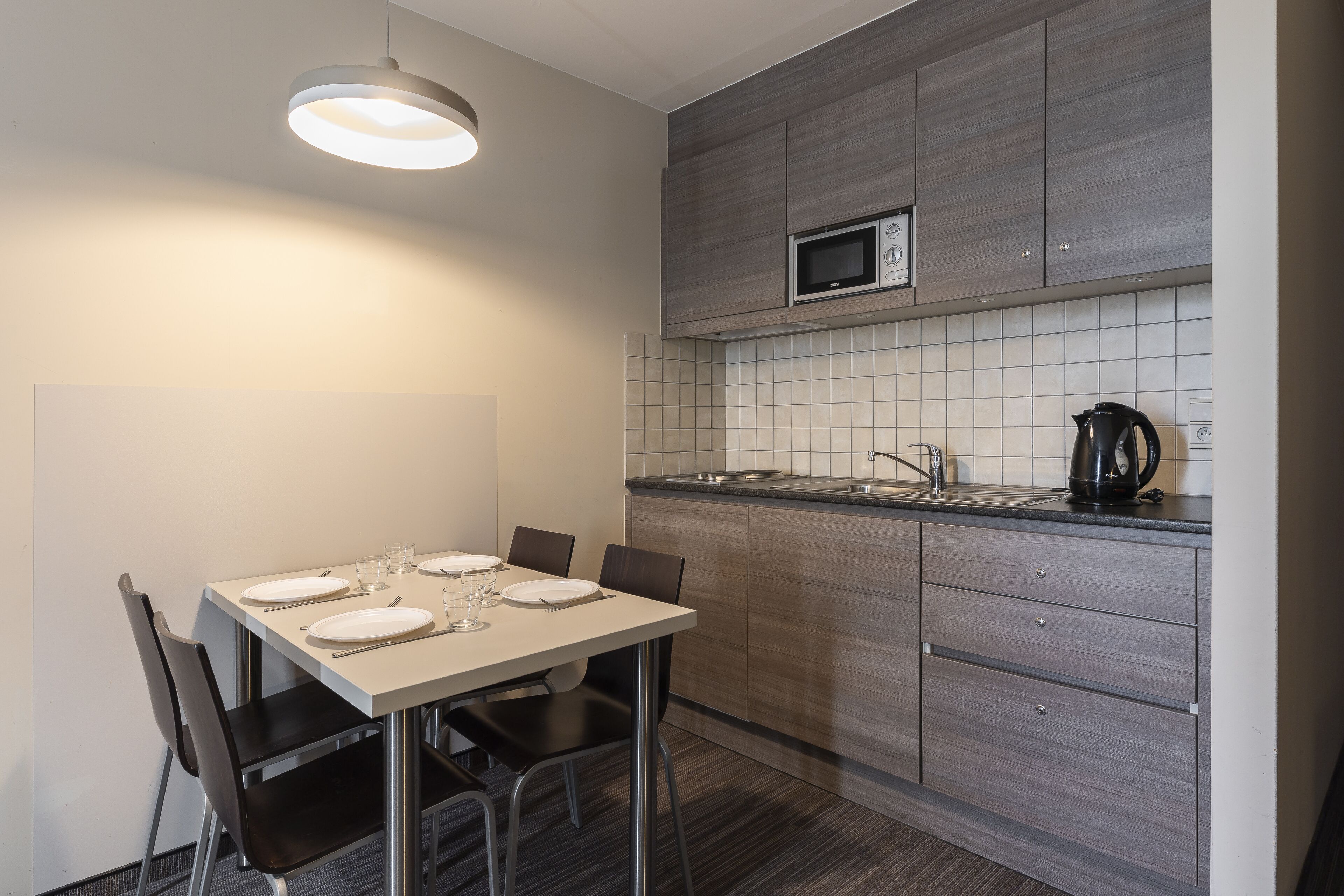 Une cuisine moderne avec une table à manger pour quatre personnes, un four à micro-ondes et une bouilloire posés sur le plan de travail.