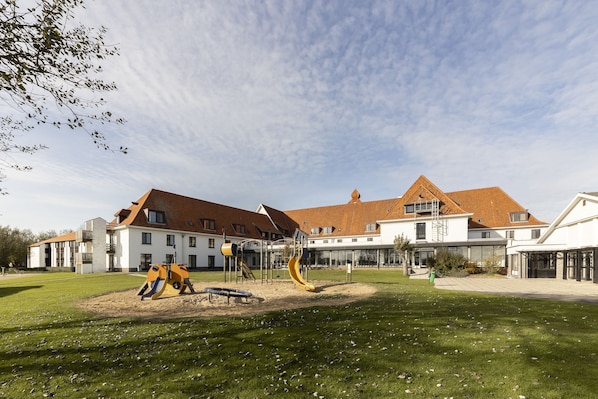 A playground with slides and climbing structures, surrounded by a well-maintained lawn and a building with a red-tiled roof.