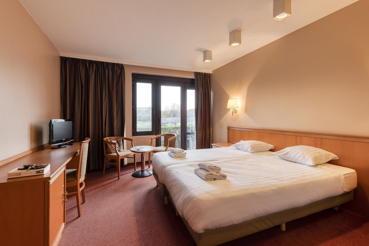Une chambre d’hôtel avec un lit, un bureau avec une télévision, une chaise et une petite table.