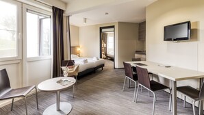 Een hotelkamer met een bed, een bureau, stoelen, een televisie en een raam met gordijnen.