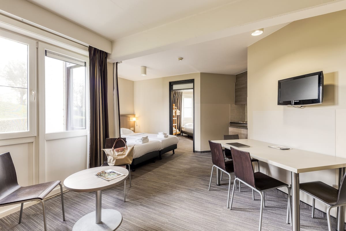 Une chambre d’hôtel avec un lit, un bureau, des chaises, une télévision et une fenêtre avec des rideaux.