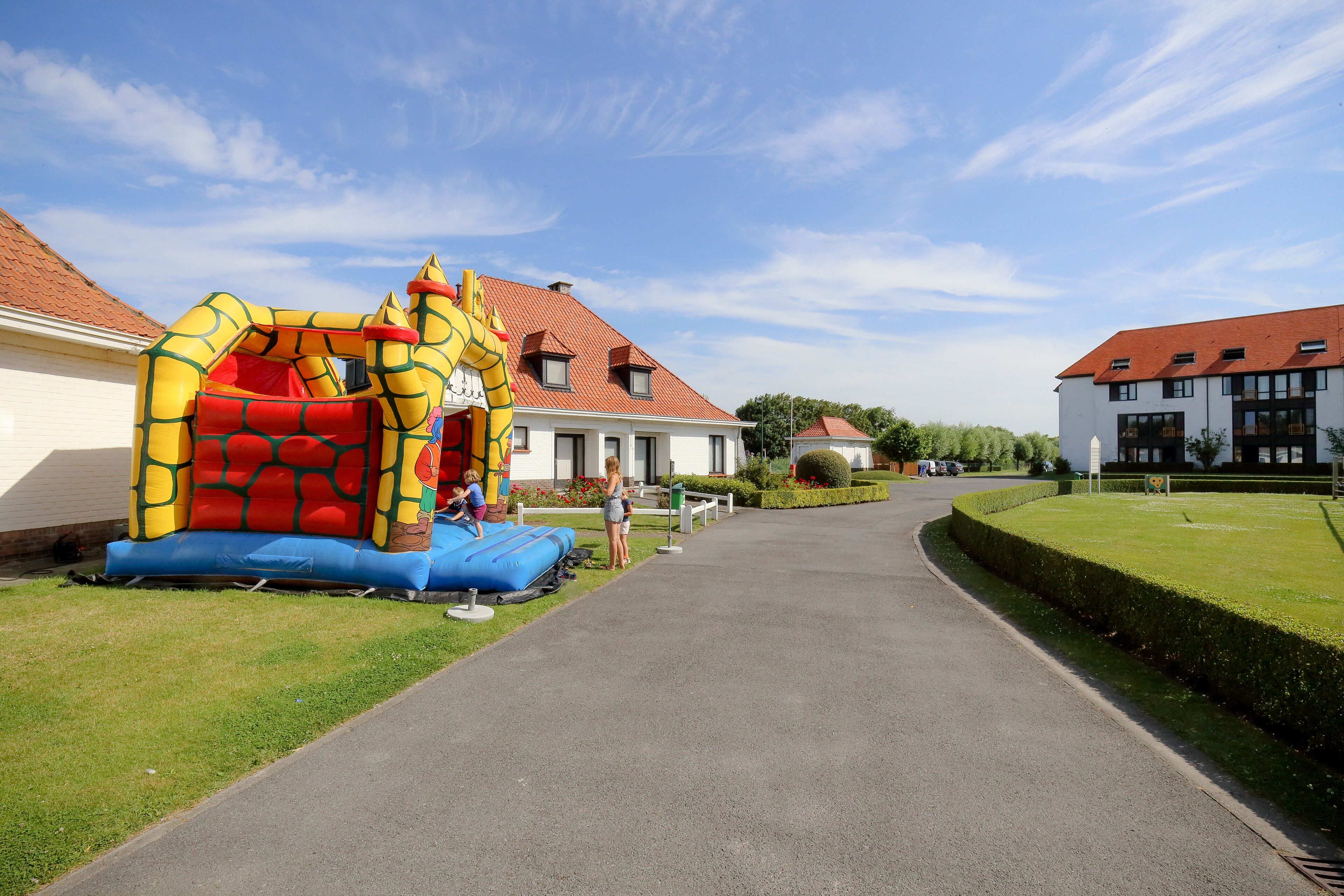 Un camino que lleva a una zona residencial con una casa de techo rojo y una estructura inflable grande para juegos.