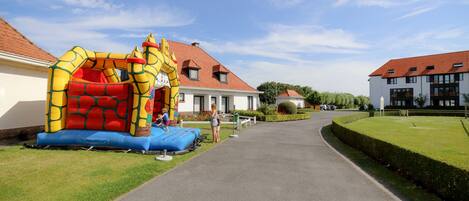 Un camino que lleva a una zona residencial con una casa de techo rojo y una estructura inflable grande para juegos.