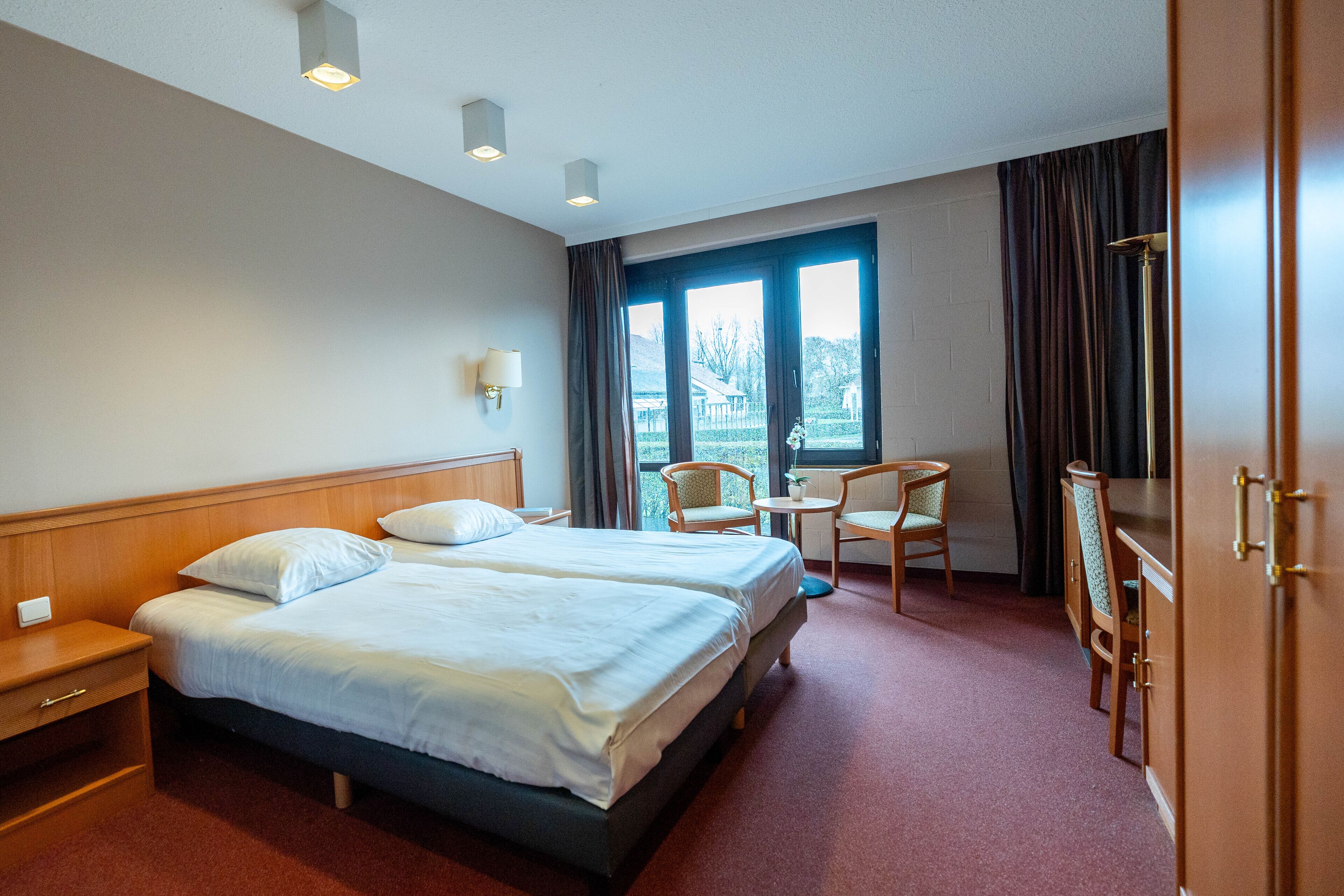 Habitación de hotel con dos camas, un escritorio, sillas, una lámpara y vistas al exterior.