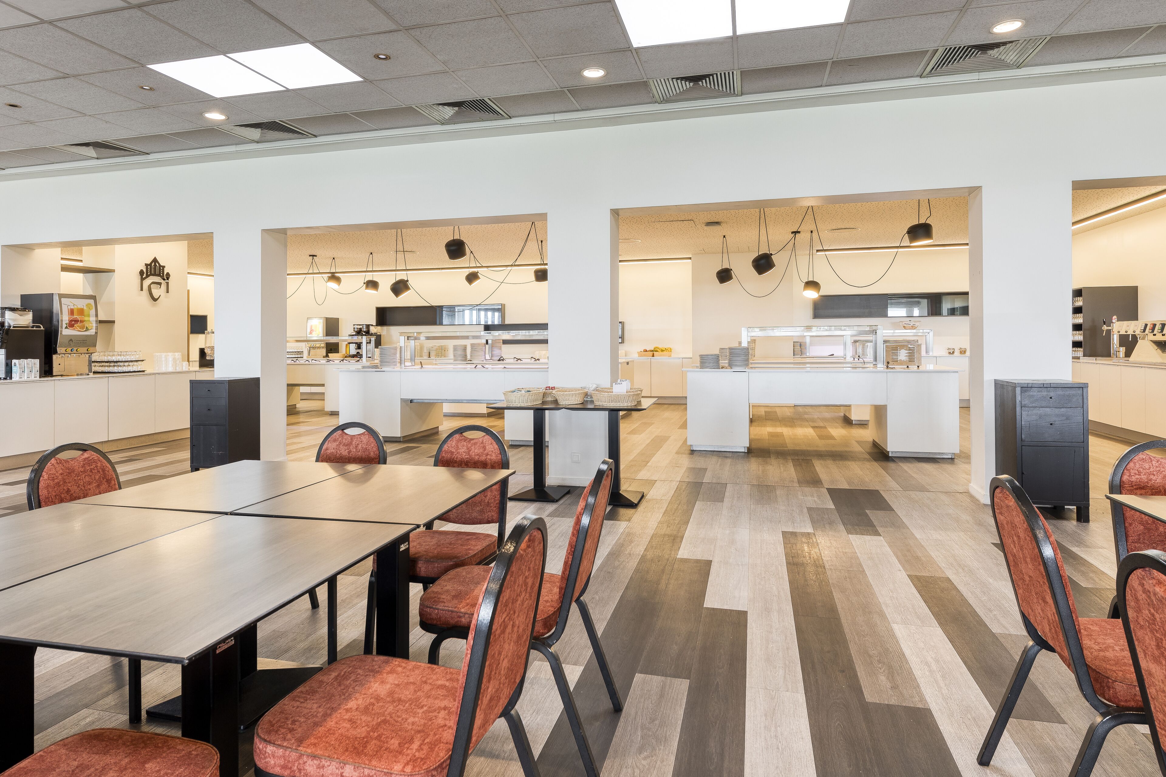 A modern dining area with a long table and chairs, kitchen area with appliances, and a clean, well-lit space.