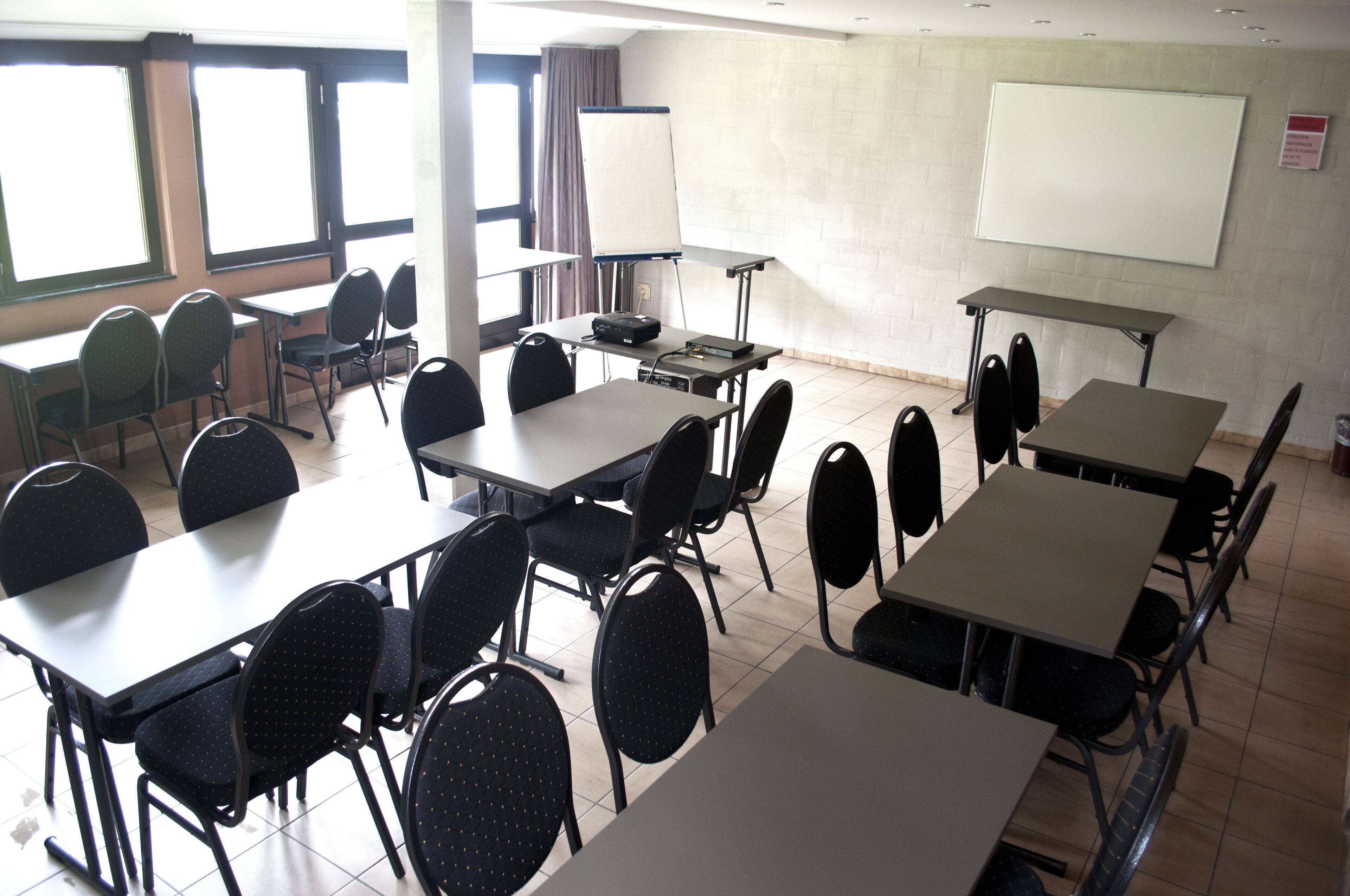 A conference room with multiple tables and chairs, a whiteboard, and a projector.