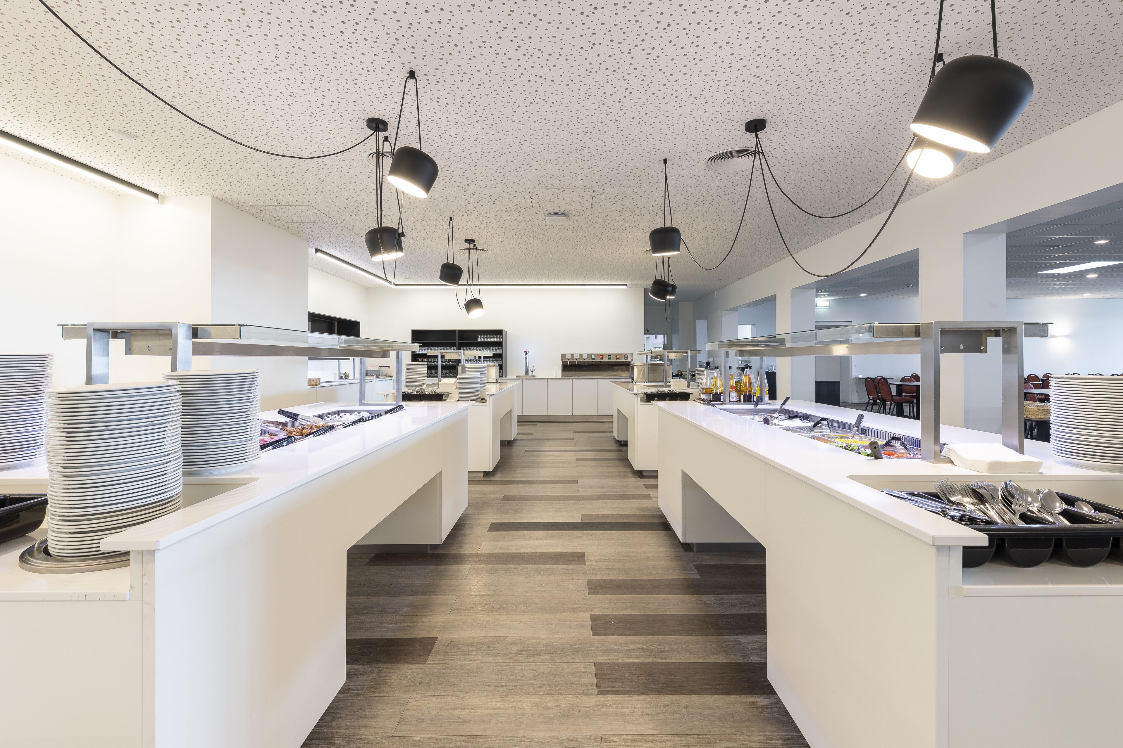 Um café moderno e espaçoso, com balcões brancos e luminárias pendentes pretas.