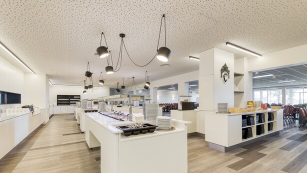 Een modern, goed verlicht café met een centrale bedieningsbar, een zithoek en een groot raam voor natuurlijk licht.