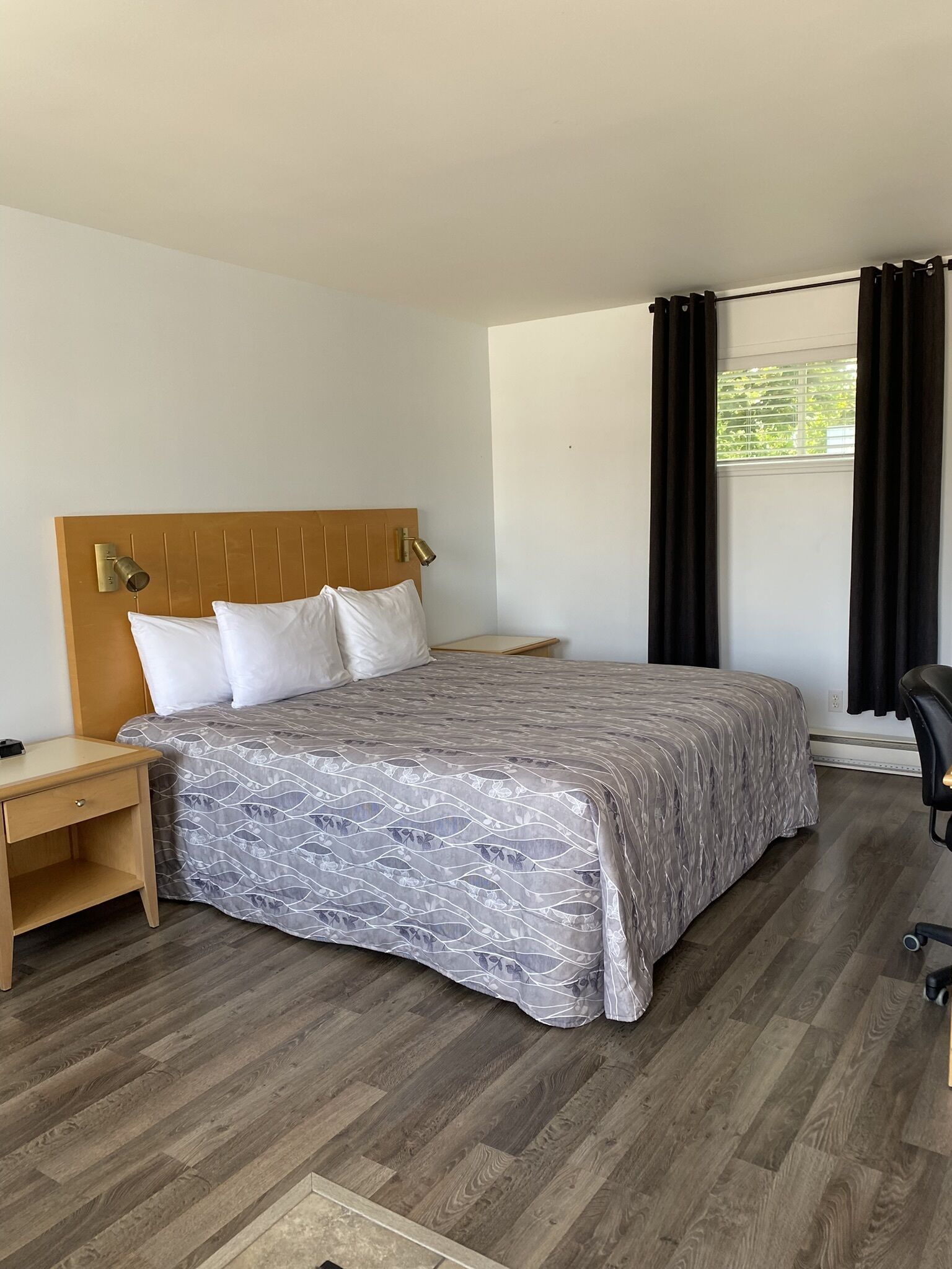 A neatly arranged bedroom with a wooden headboard, a bed with a patterned bedspread, a nightstand, a desk, and a chair.