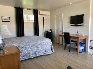 A hotel room with a bed, a desk, a chair, a television, and a window with curtains. - Motel Centre-Ville (Montmagny)