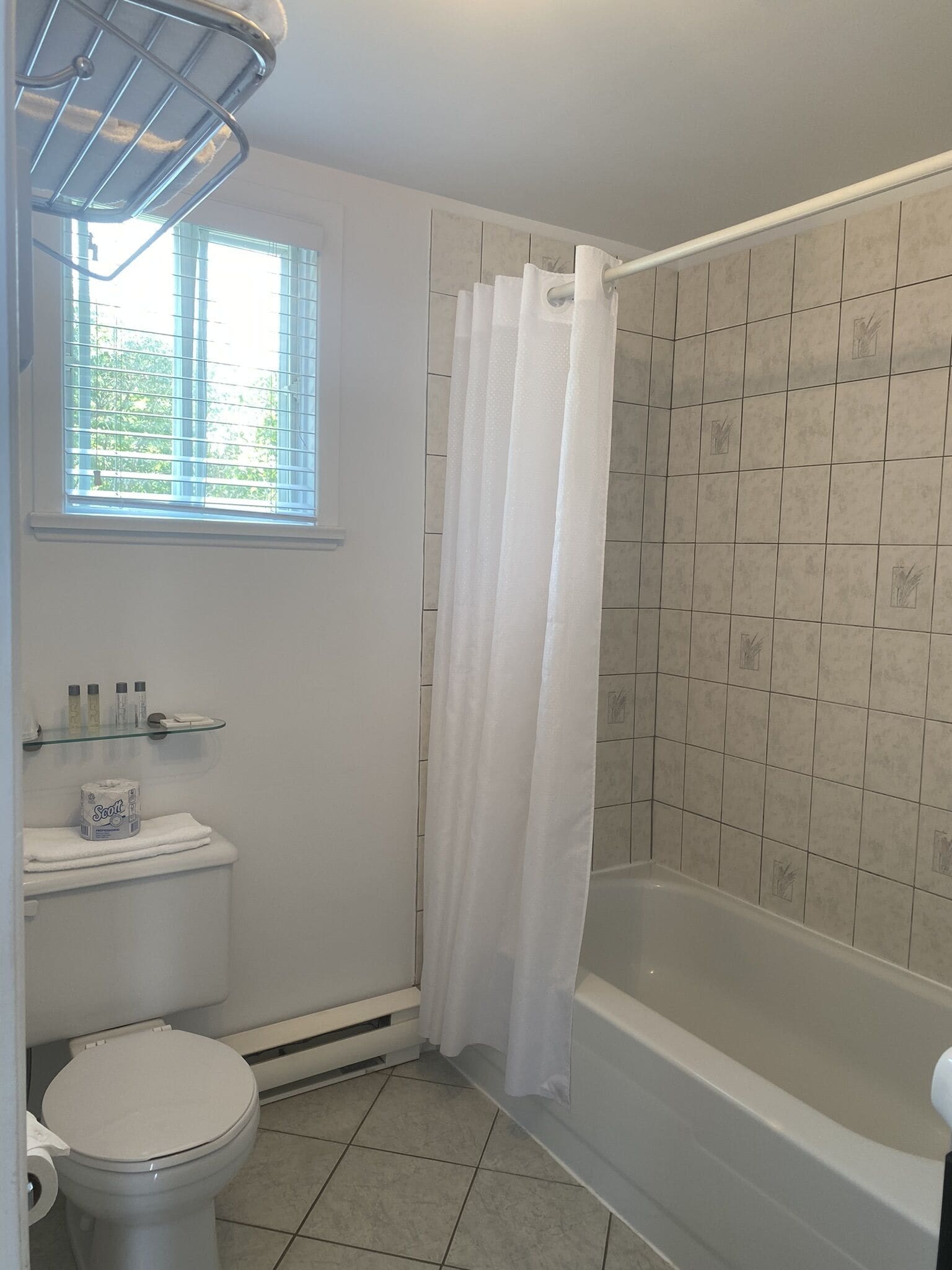 Un baño con inodoro, ducha con cortina blanca, bañera y ventana con persianas.