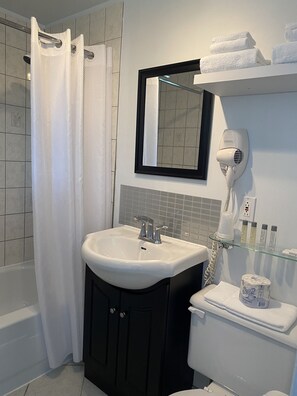 A bathroom with a white sink, black cabinets, a glass shower enclosure, a white toilet, and a towel rack with towels. - Motel Centre-Ville (Montmagny)
