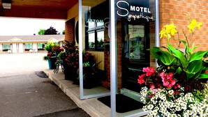 Entrada de motel com fachada de tijolos, janelas amplas e plantas em vasos.
