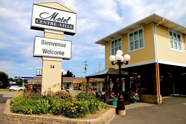 A motel sign with 'Motel Centre-Ville' and 'Bienvenue Welcome' in front of a building with a covered entrance and a lamp post. - Motel Centre-Ville (Montmagny)