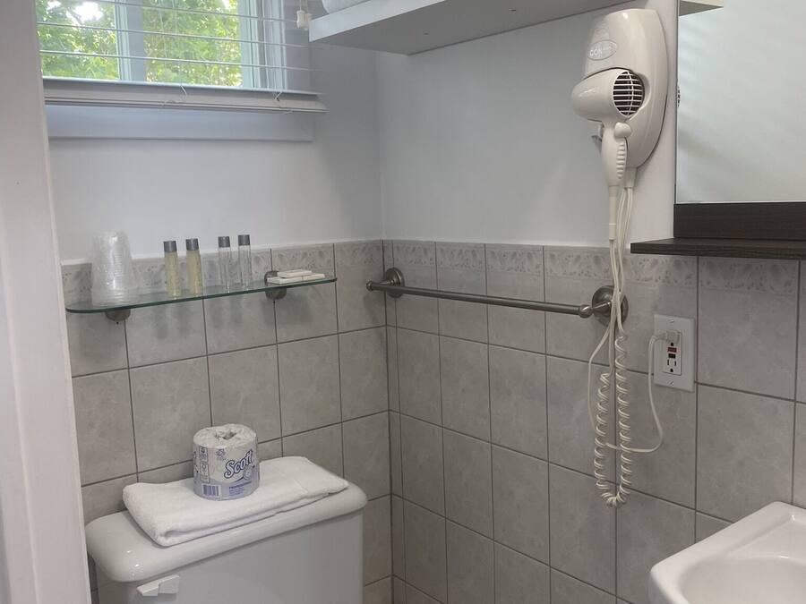 Ein Badezimmer mit Toilette, einem Handtrockner, einer Ablage mit Handtüchern und einem Fenster mit Jalousien.