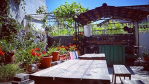 Une terrasse extérieure avec des bancs et des tables en bois, entourée de plantes et de fleurs en pot.