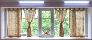 A window with two curtains tied back, revealing a view of greenery outside. - JR's House - Hostel (Yerevan)