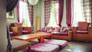 Un salon avec un canapé, des fauteuils, une table et une grande fenêtre avec des rideaux.