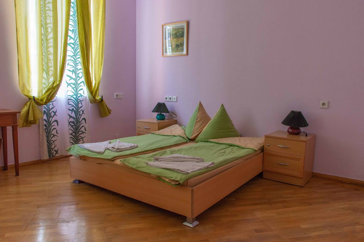 A bedroom with a bed, two bedside tables, a nightstand, a lamp, and a window with curtains.