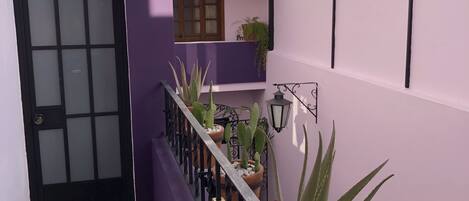 Un pasillo estrecho con una pared morada, una puerta negra y un suelo de baldosas.