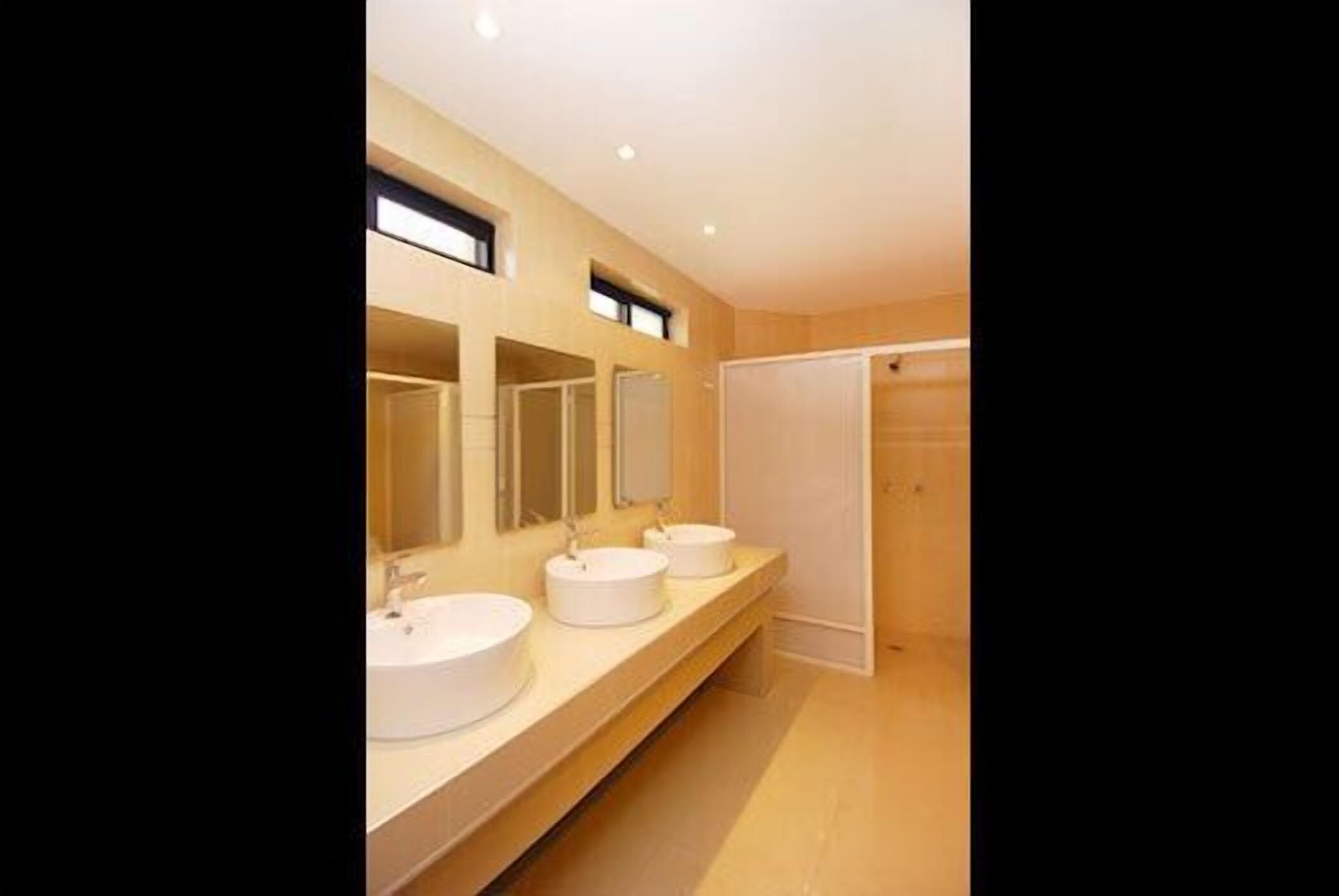 Baño con tres lavamanos, espejos grandes y zona de ducha.