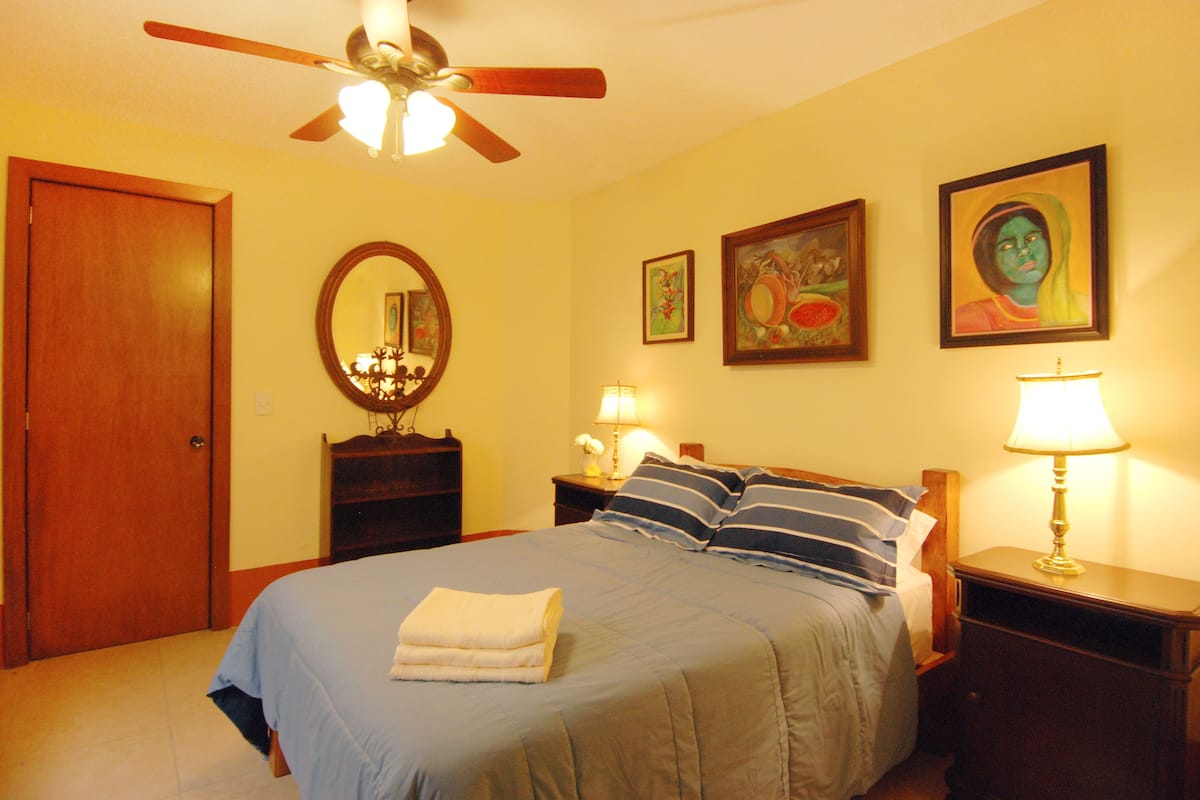 Quarto com cama, ventoinha no teto, espelho e duas mesas de cabeceira com luminárias.