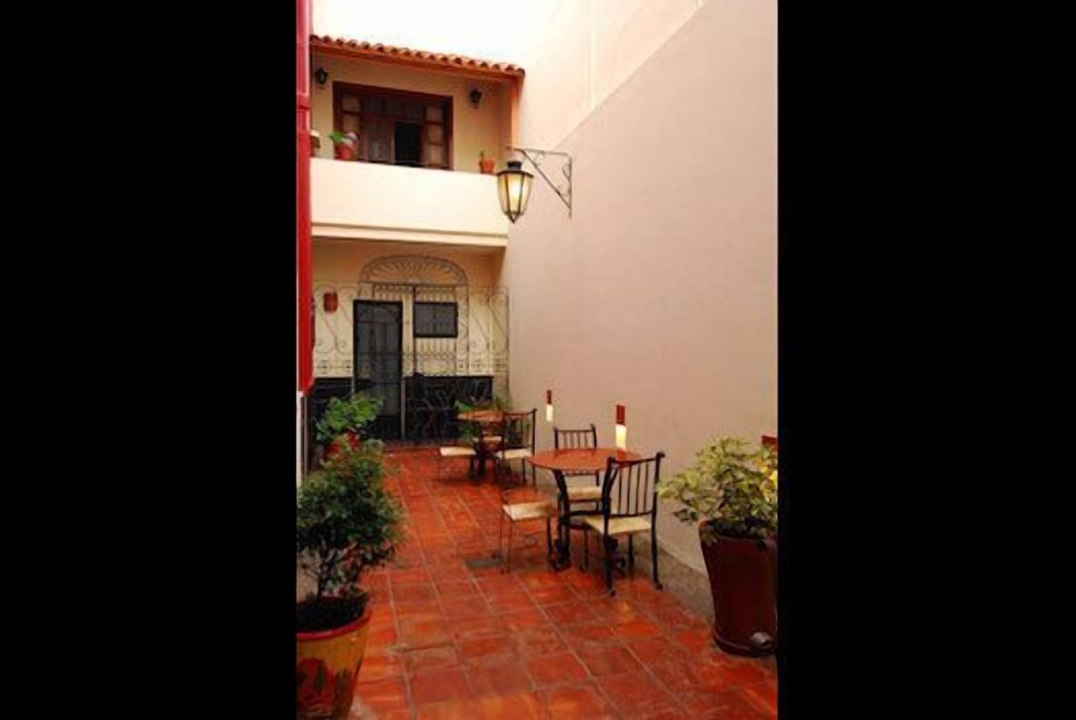 A courtyard with a tiled floor, a dining area with tables and chairs, and a building entrance with a door.