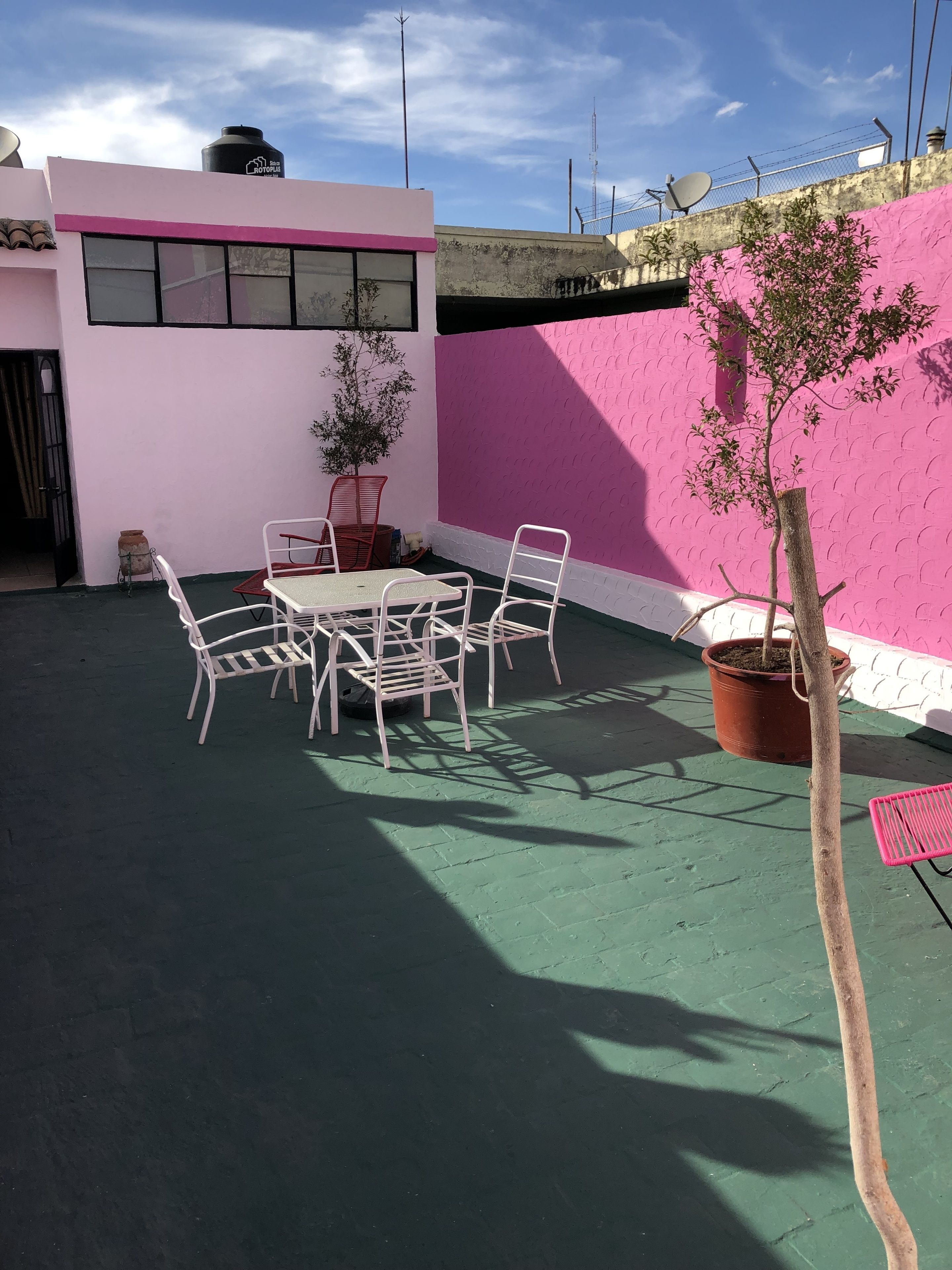 Eine Terrasse mit Tisch und Stühlen, einem Blumentopfbaum und einer rosafarbenen Wand.