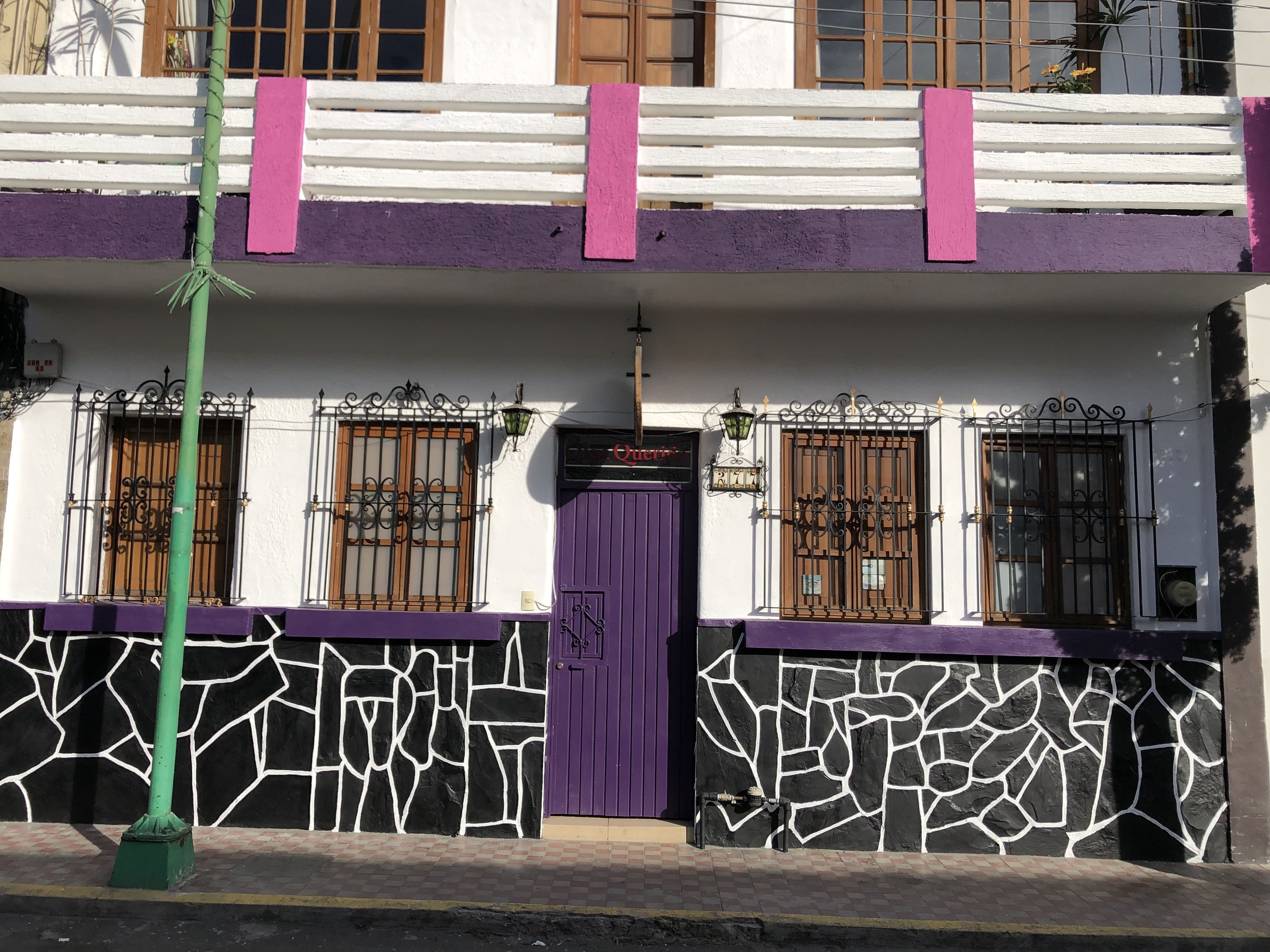 Un bâtiment avec une porte et des fenêtres violettes, une façade qui ressemble à de la pierre et un poteau vert devant.