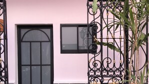 Una puerta negra con un ventanal encima, un banco con cojín estampado, y un portón metálico decorativo con plantas.