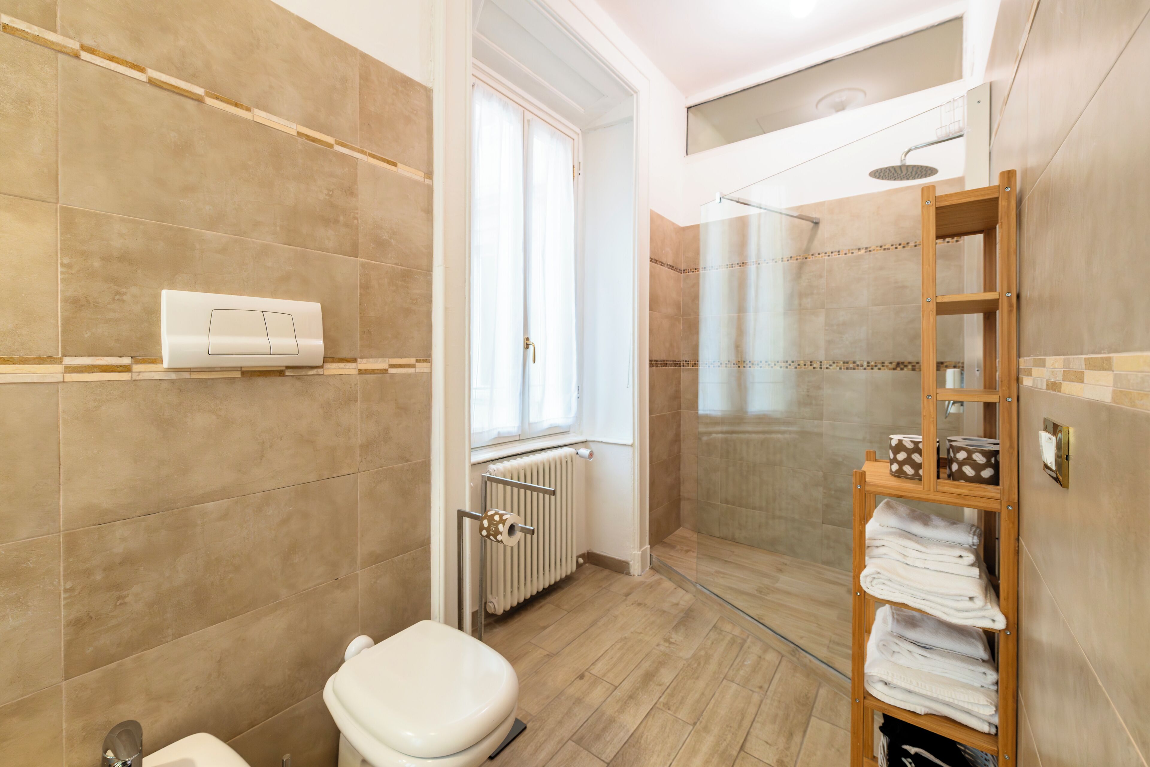 A modern bathroom with a toilet, shower, and a wooden shelf with towels.