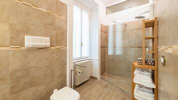 A modern bathroom with a toilet, shower, and a wooden shelf with towels.