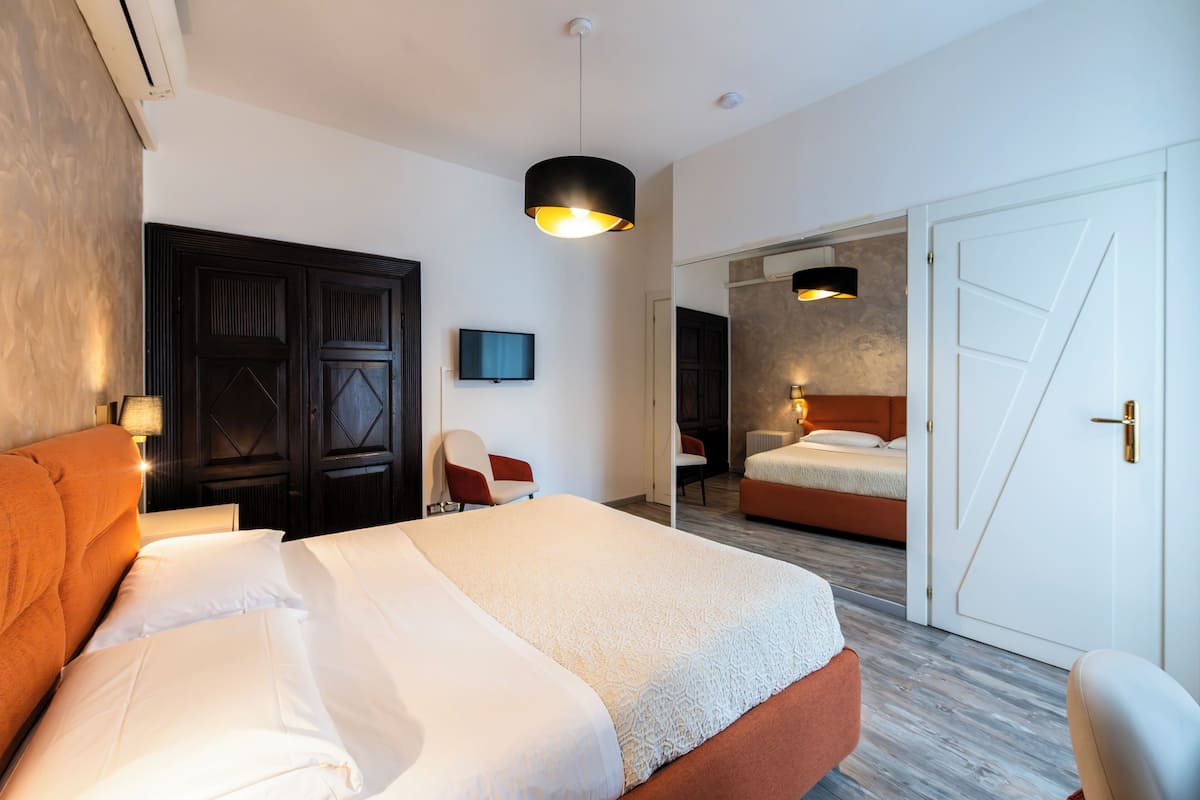 A hotel room with a large bed, a chair, a desk, and a wardrobe.