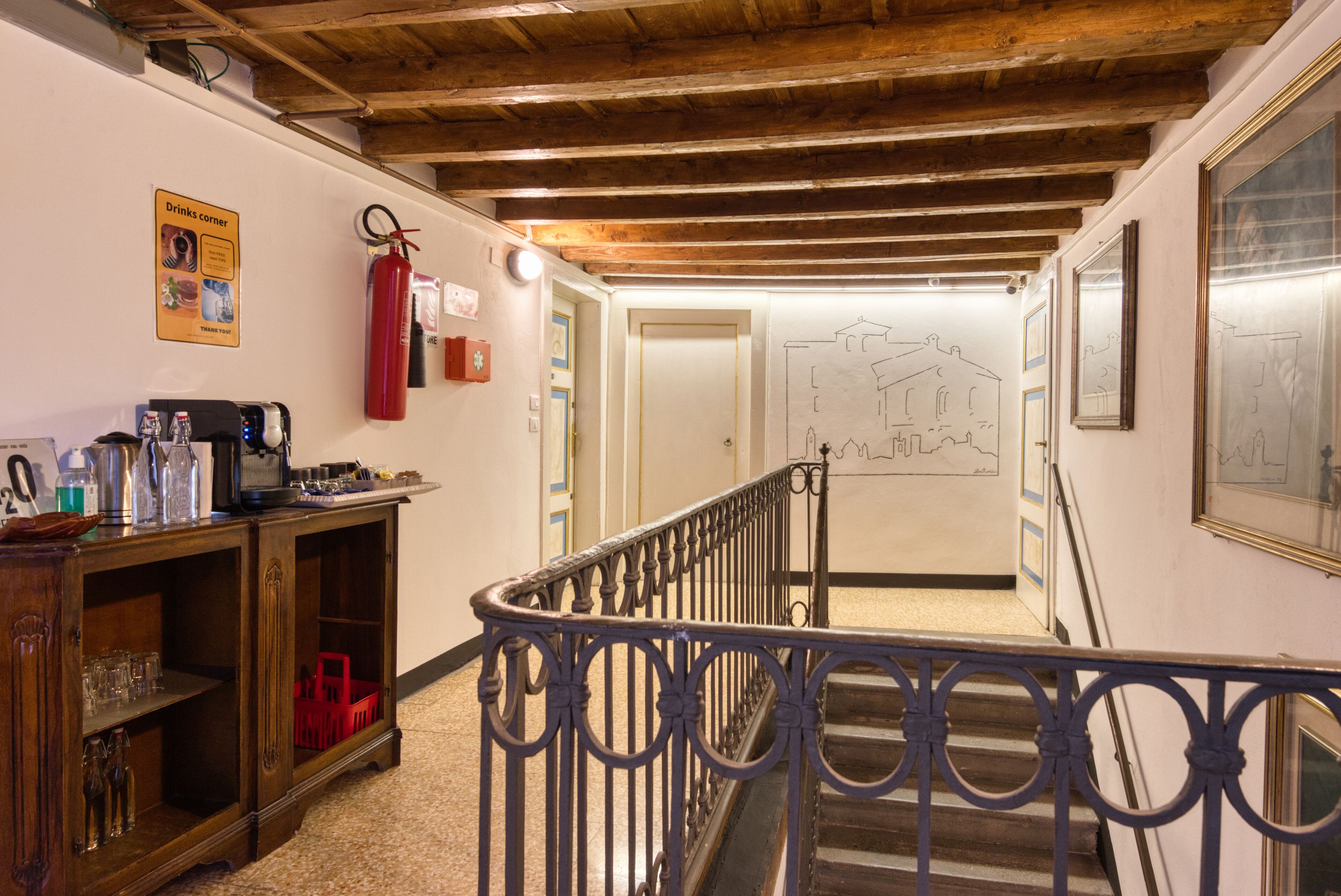 A hallway with a wooden ceiling, a staircase with ornate metal railings, and a drinks corner with various bottles and glasses.