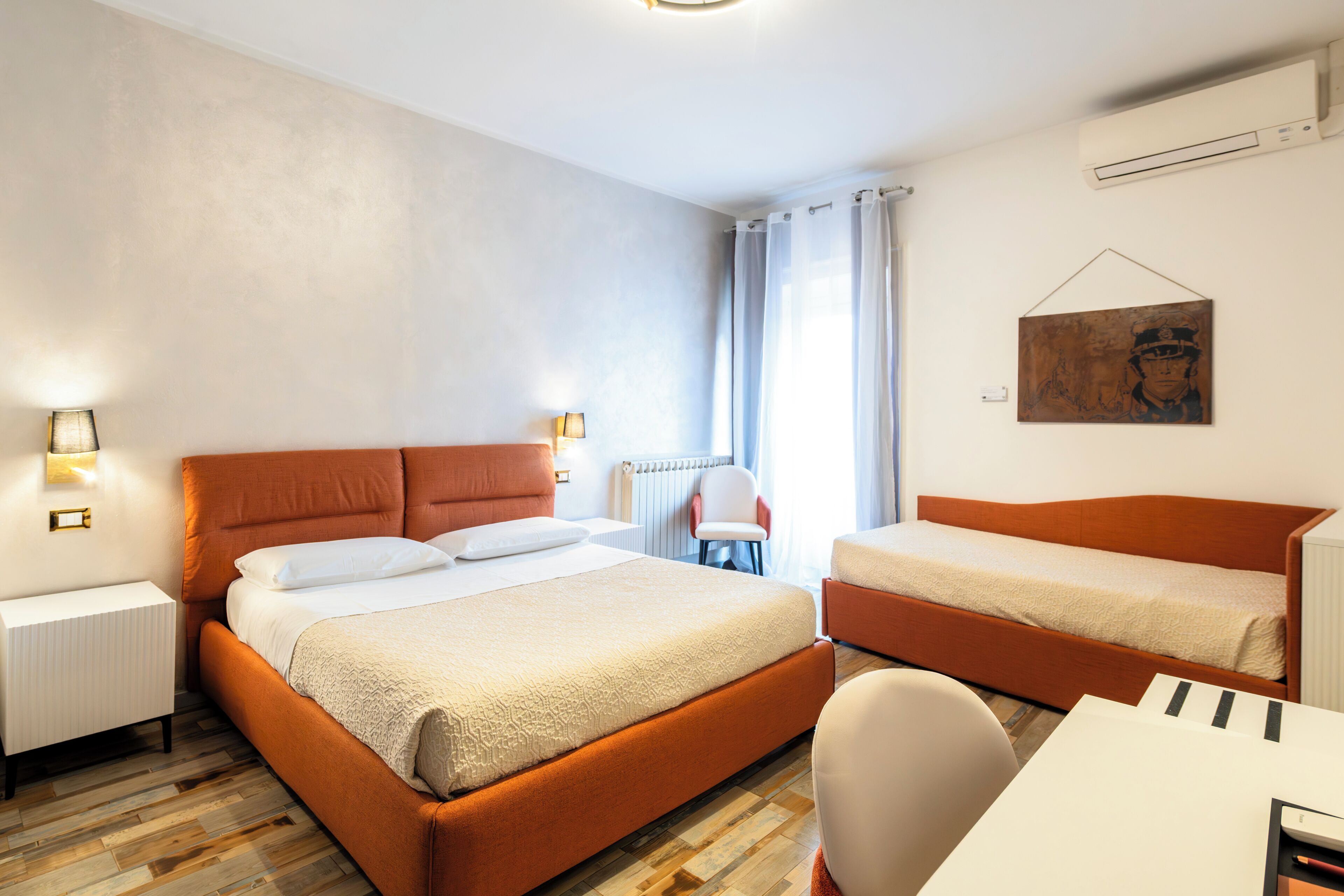 Habitació d'hotel amb un llit gran, un llit més petit, una taula i una cadira.