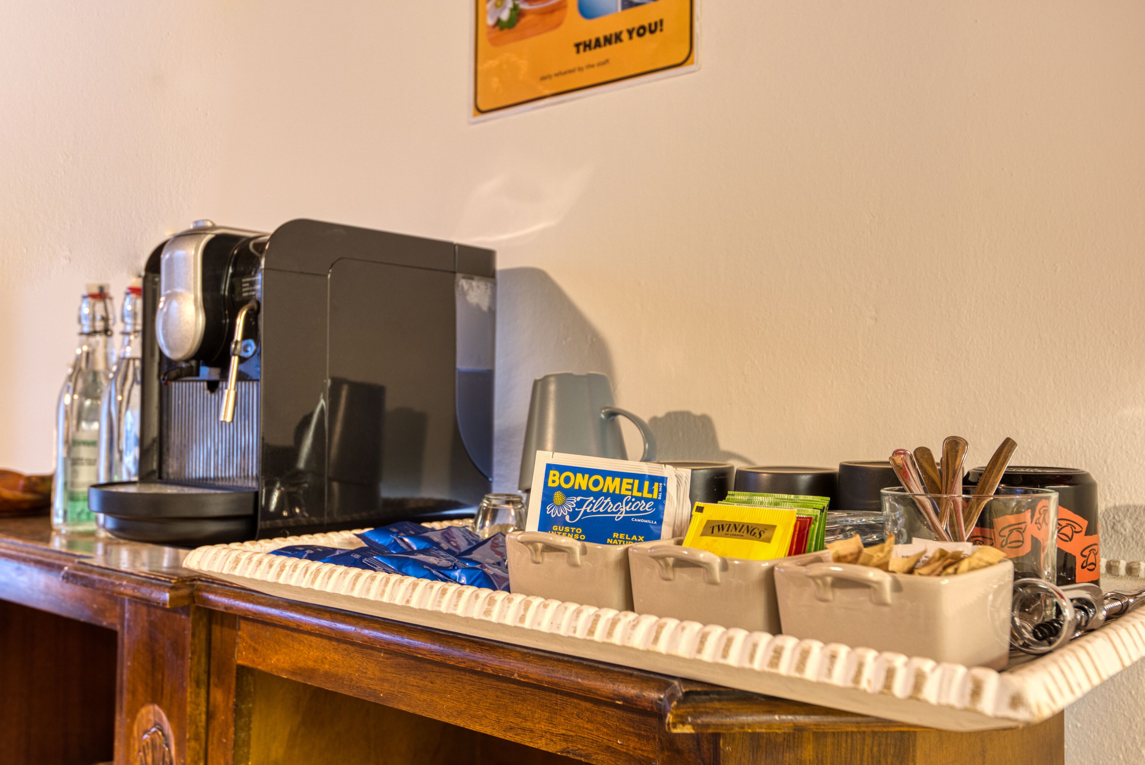 A hotel reception area with a coffee machine, a tray with snacks, and a sign for Bonomelli.