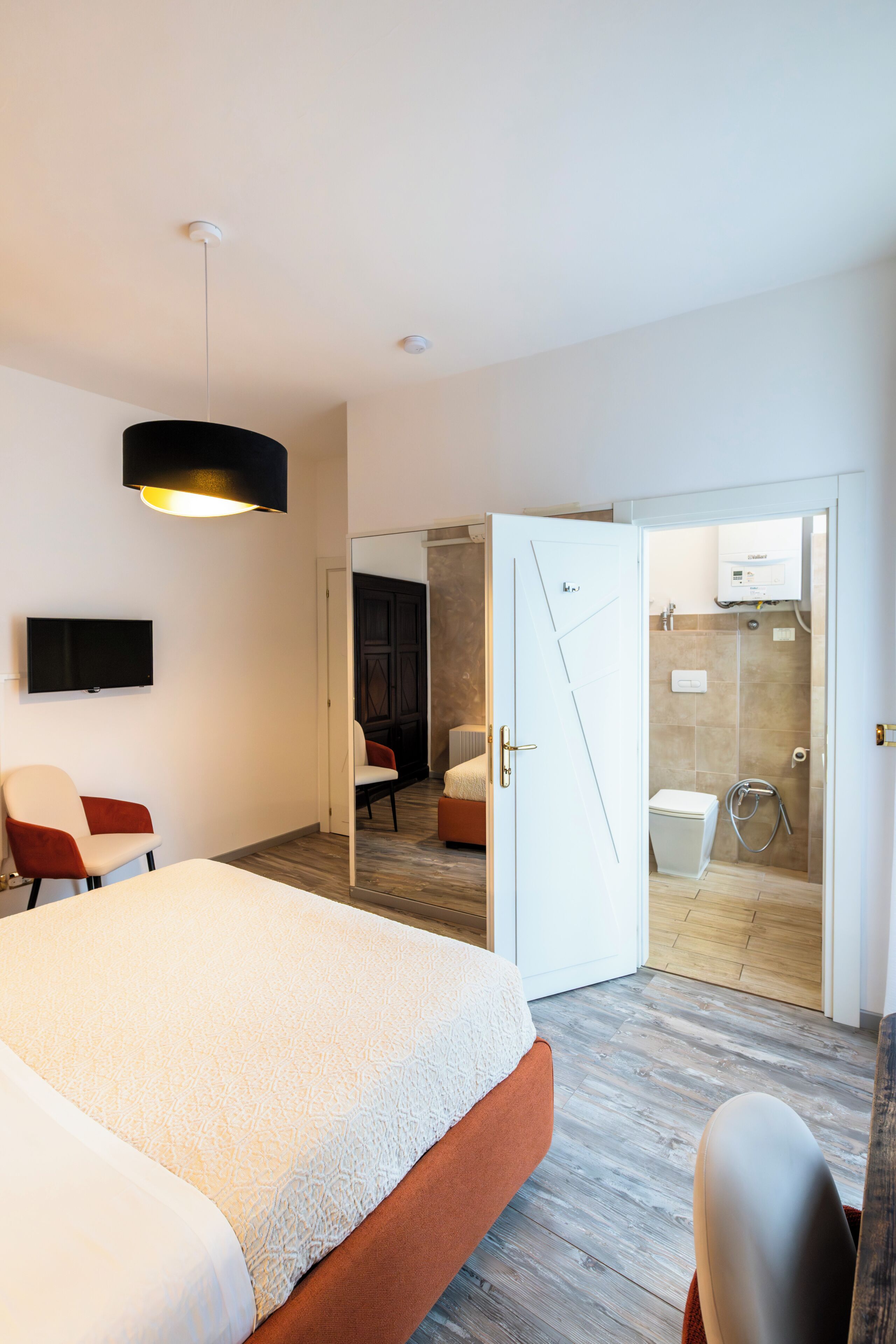 A hotel room with a bed, a TV, a chair, a door leading to a bathroom, and a shower.