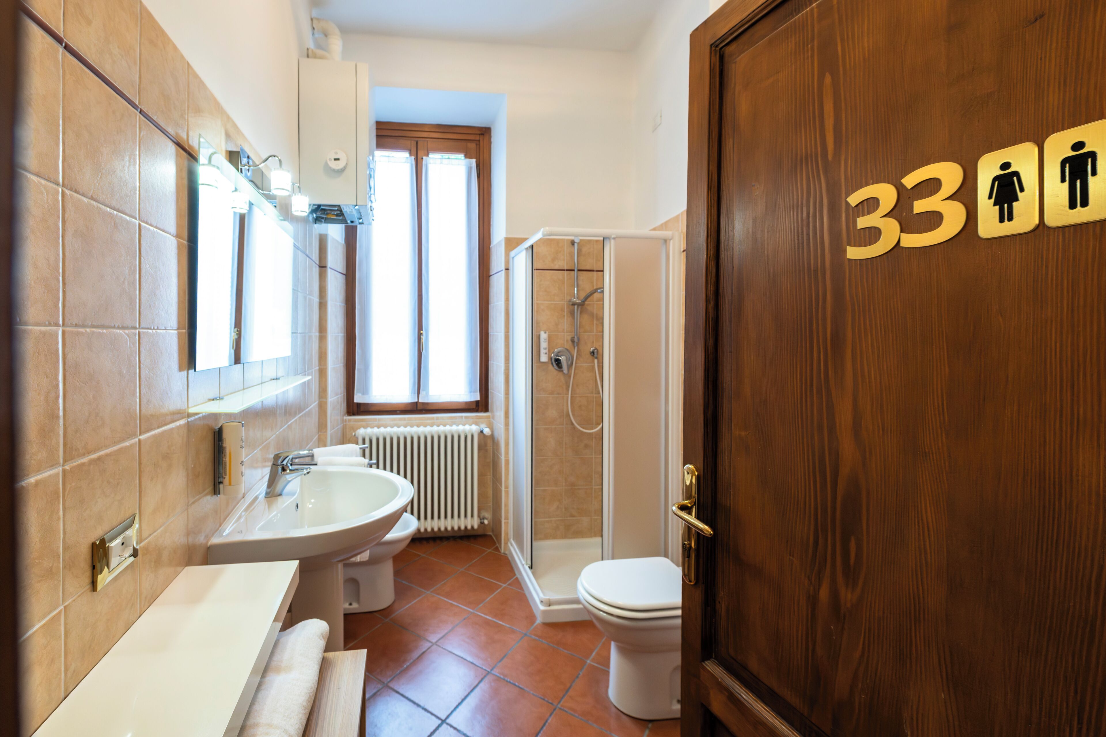 Un baño con lavamanos, inodoro y ducha. Hay una puerta con el símbolo de número 33.