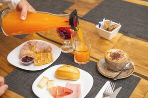 A breakfast table with a waffle, cheese, ham, a croissant, a glass of orange juice, and a cup of coffee.