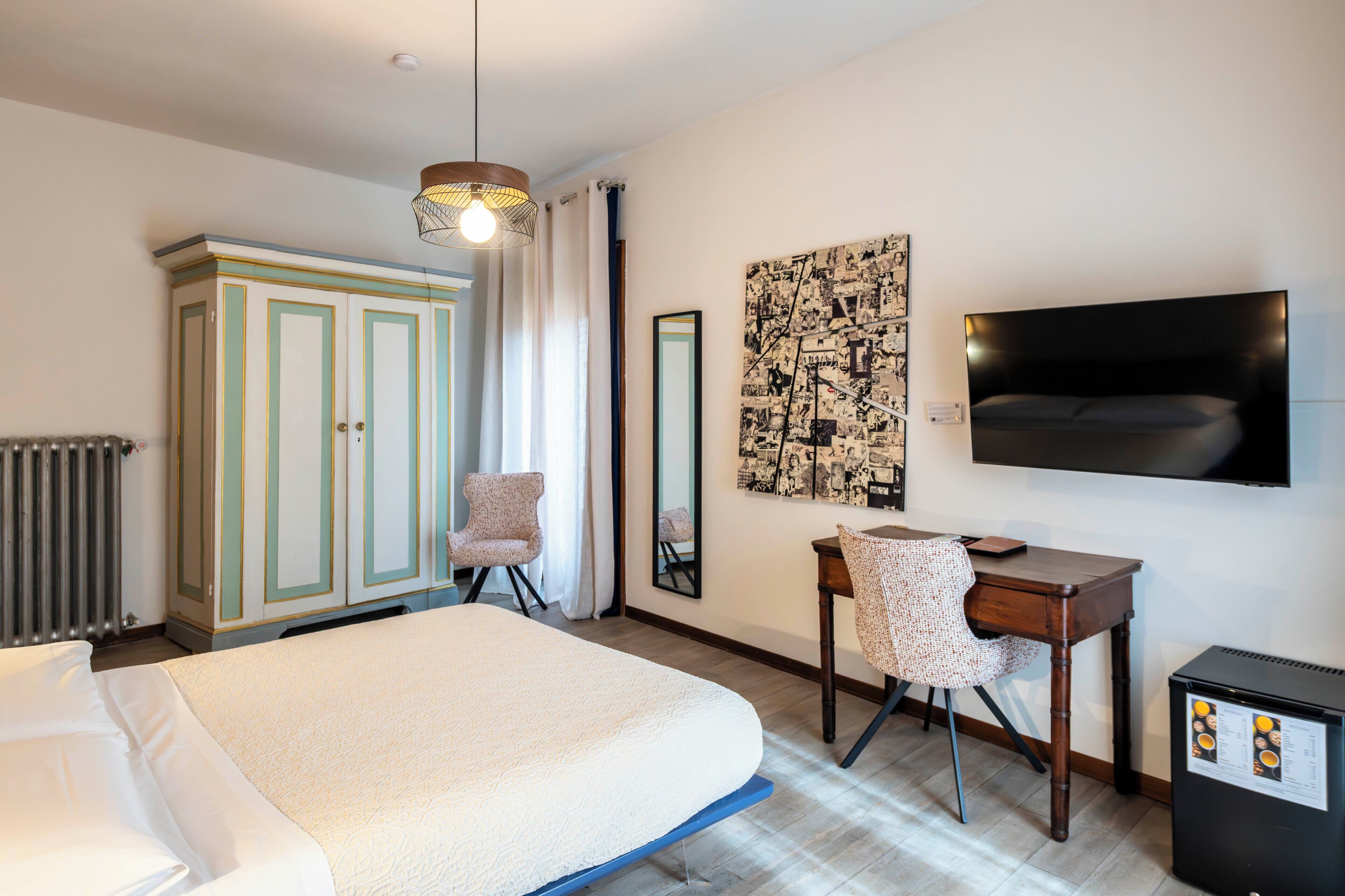 Ein Schlafzimmer mit Bett, Schreibtisch, Stuhl, Kleiderschrank, Heizkörper, Fernseher und einer Kaffeemaschine.