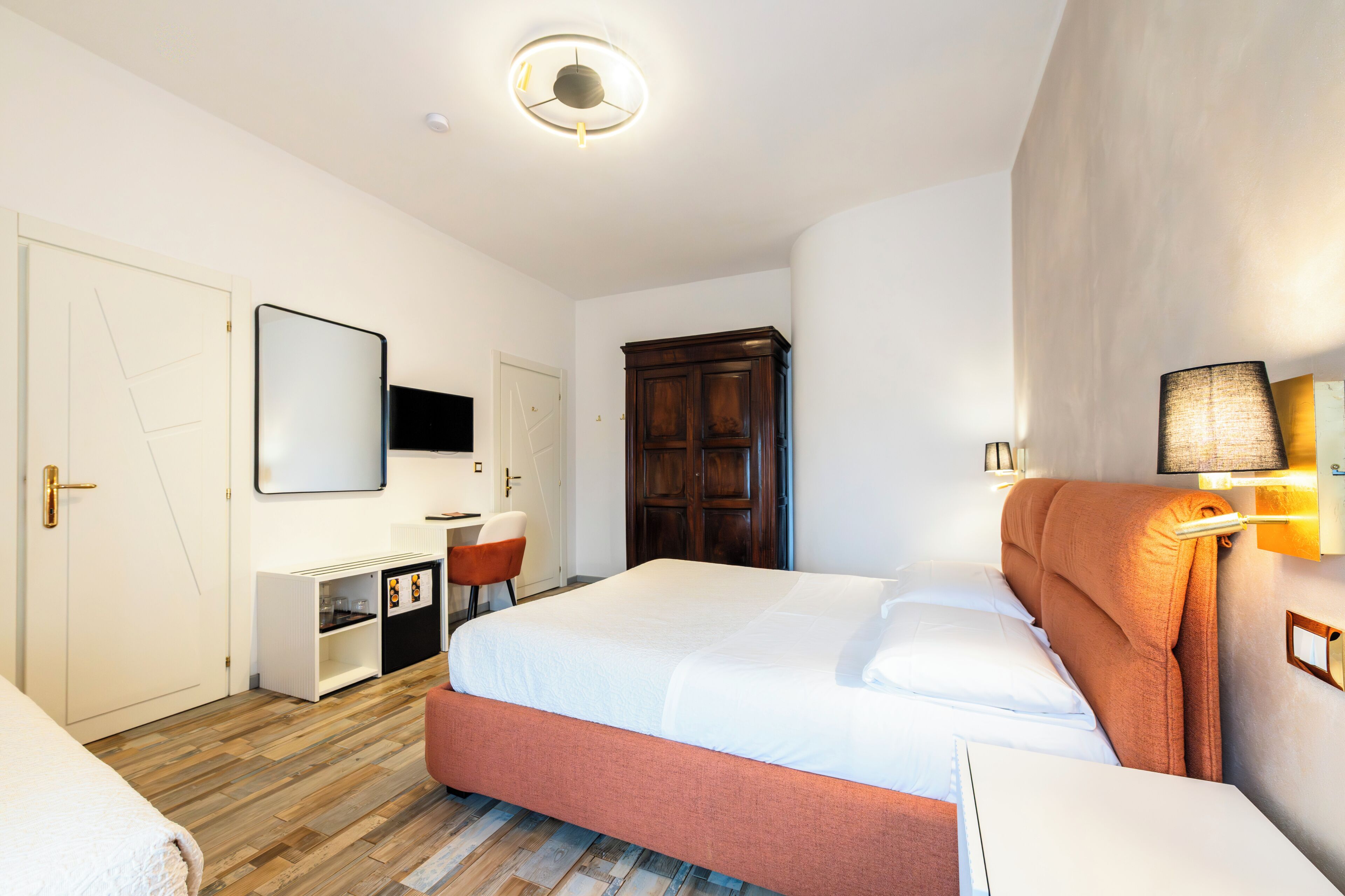 Una habitación de hotel con cama, escritorio, silla, armario y espejo.
