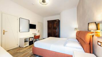 Una habitación de hotel con cama, escritorio, silla, armario y espejo.