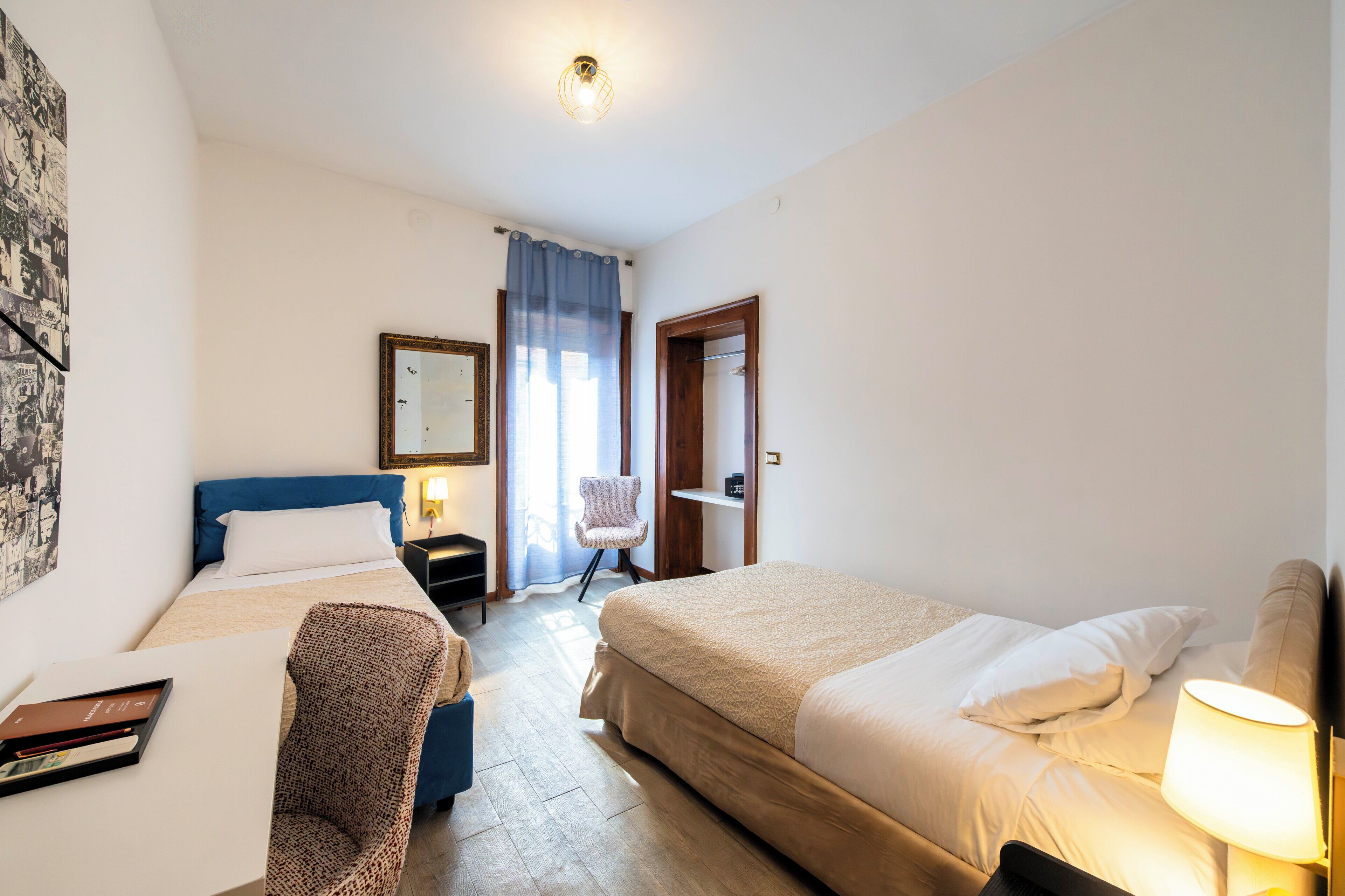 Habitación de hotel con dos camas, un escritorio, una silla, una lámpara, un espejo y una ventana con cortinas.