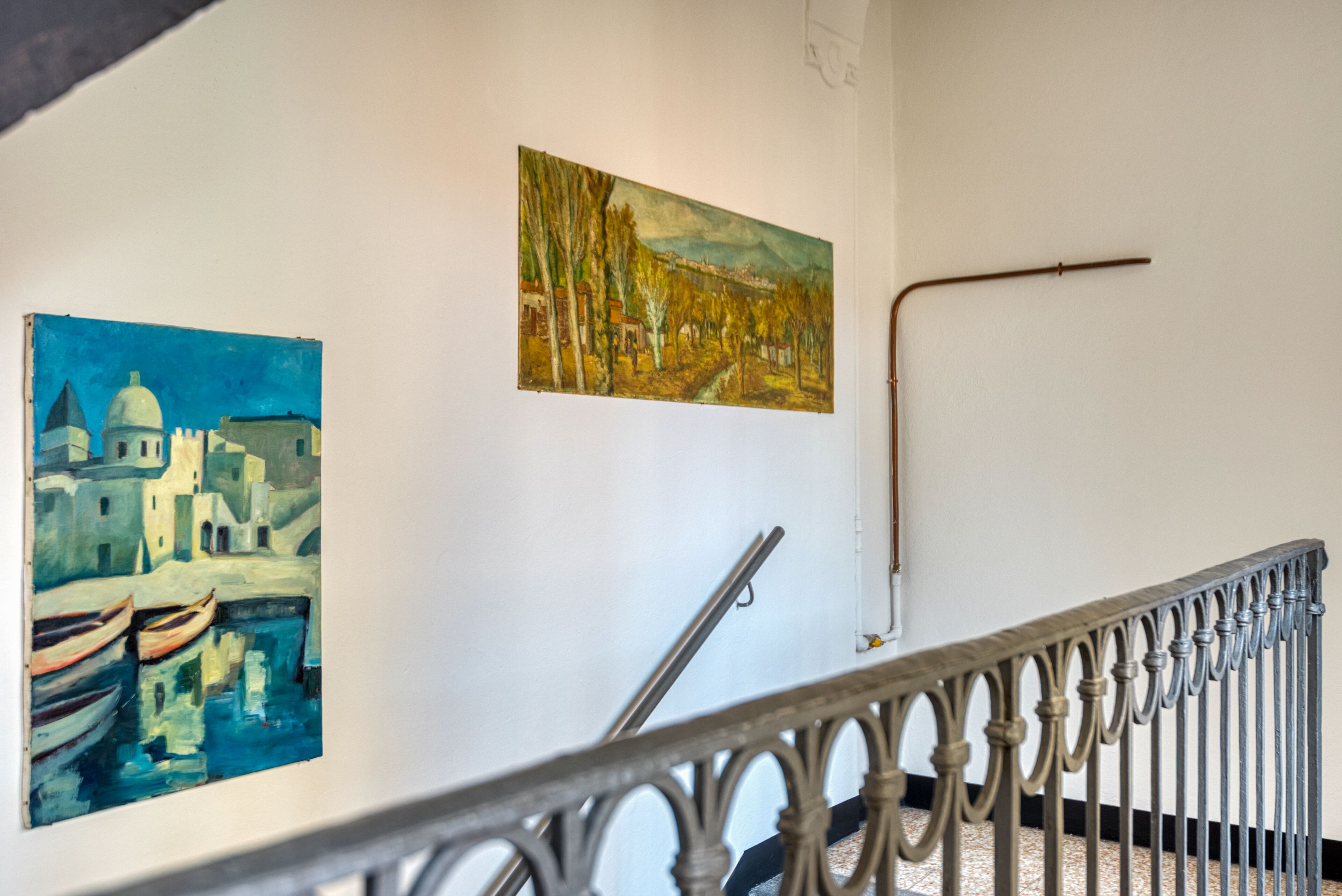 A staircase with ornate metal railings and two paintings on the wall.