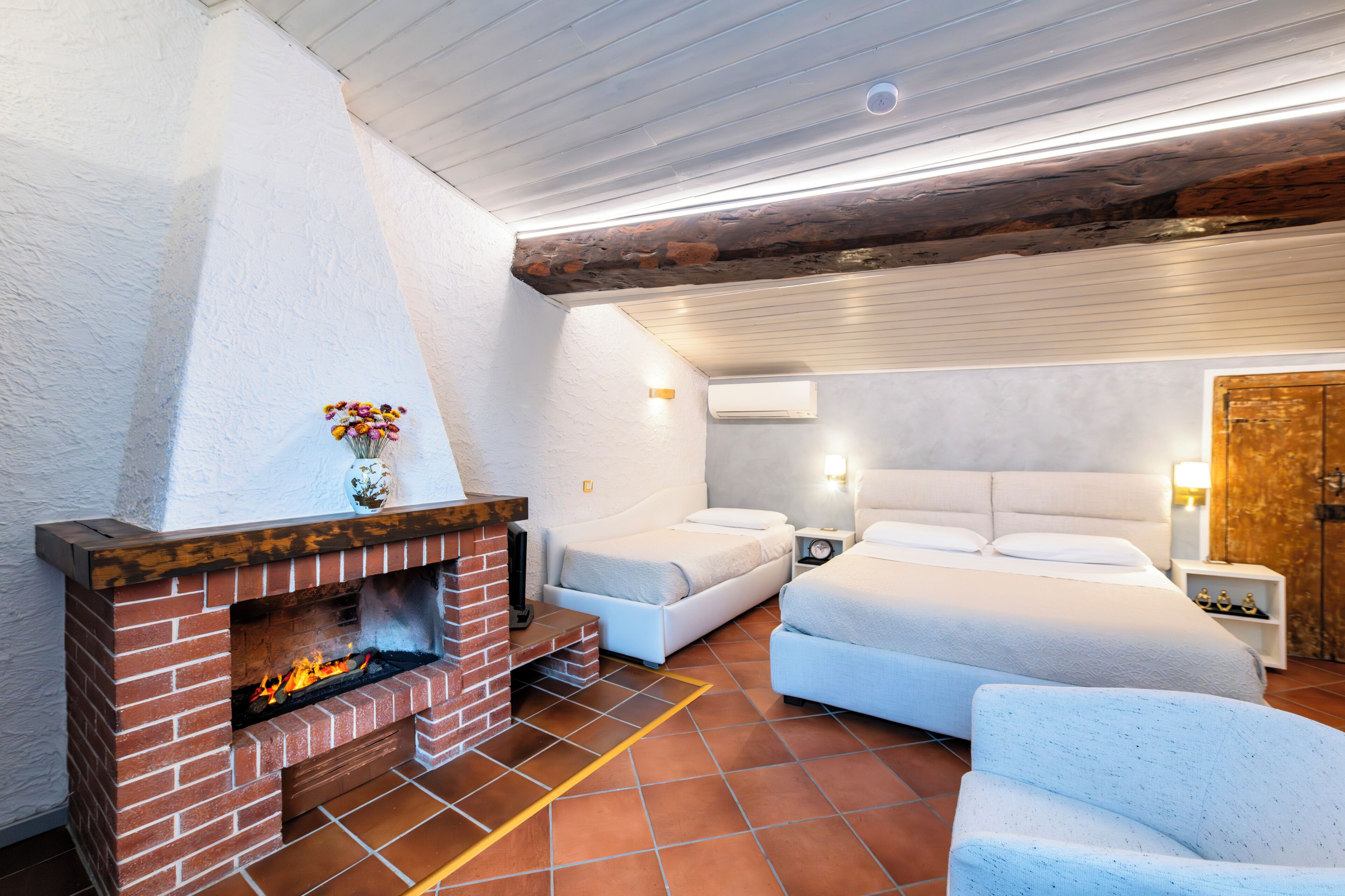 A room with a brick fireplace, two beds, a nightstand, and a wooden door.