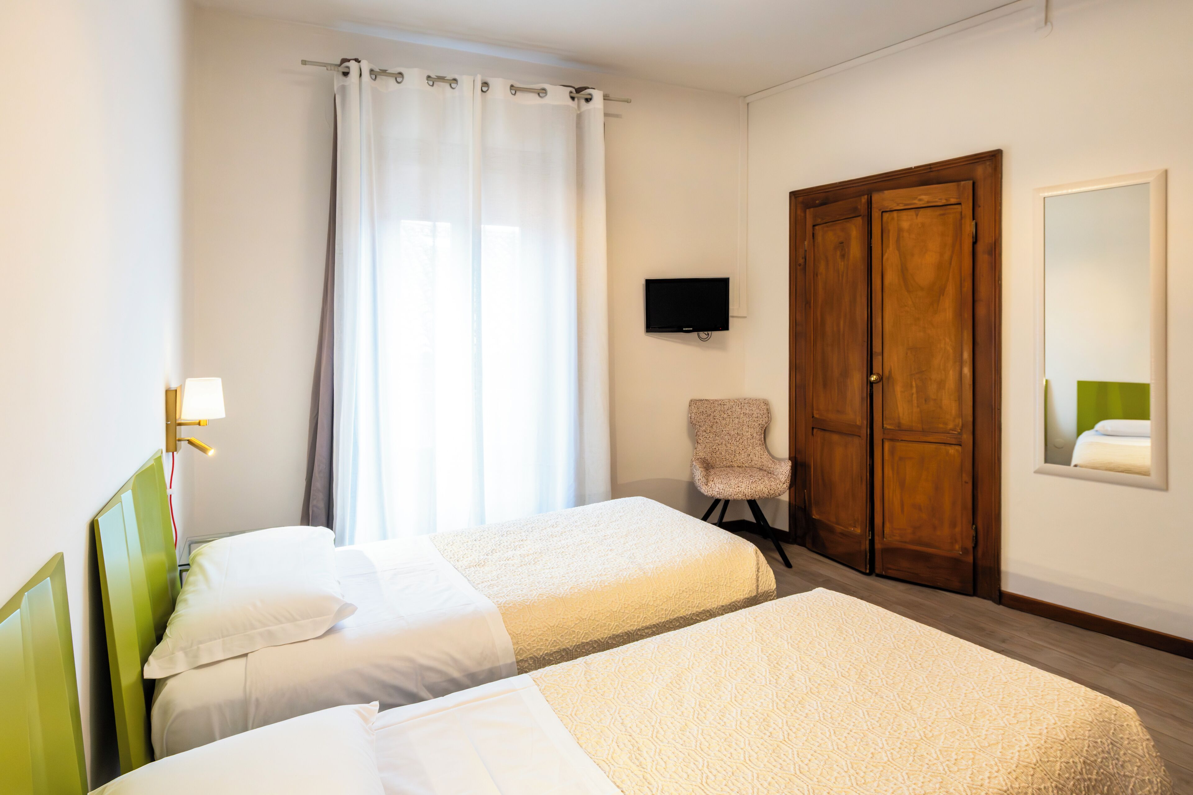 Quarto de hotel com duas camas, uma televisão, uma cadeira e um guarda-roupa de madeira.