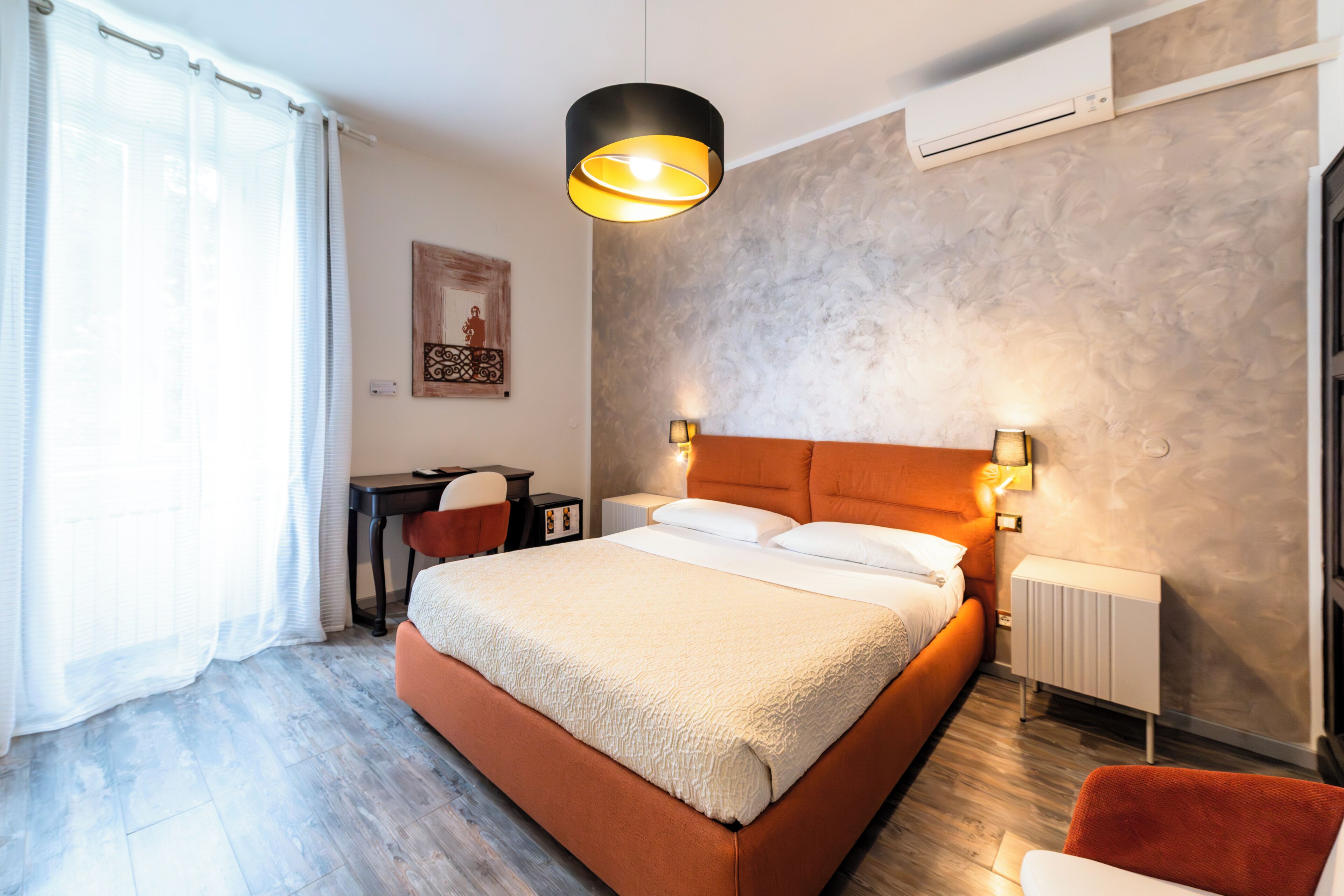 A bedroom with a large bed, a desk, a chair, a radiator, and a wall-mounted air conditioner.