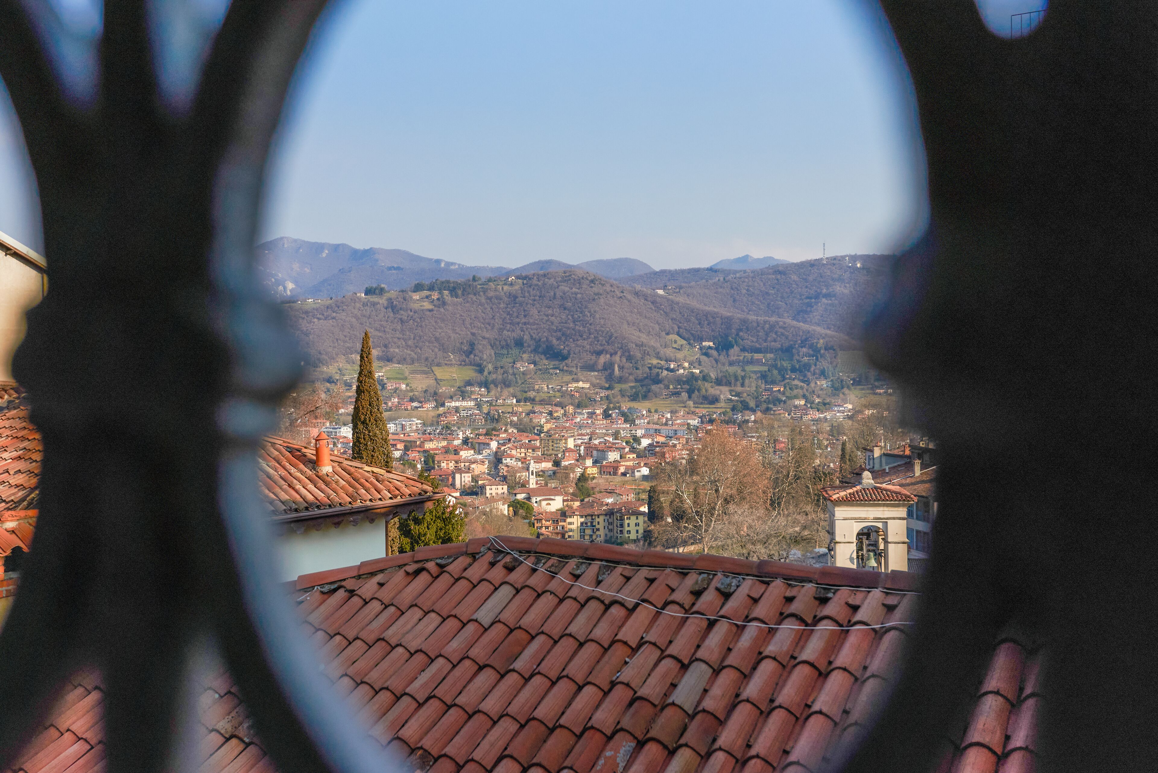 A view through a window with a tiled roof, overlooking a town with buildings and hills in the background.