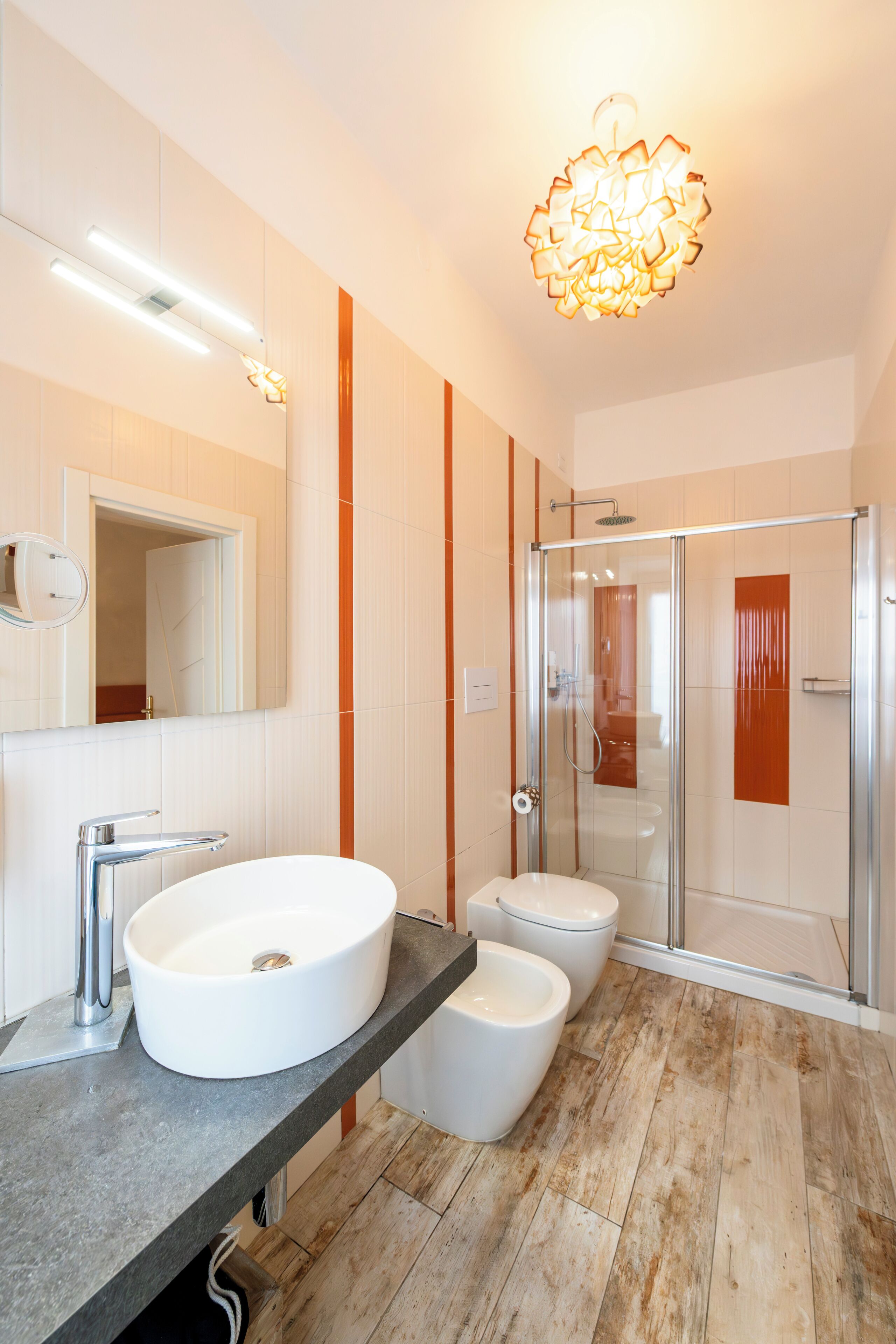 A modern bathroom with a large white sink, a bidet, a glass shower enclosure, and a mirror.